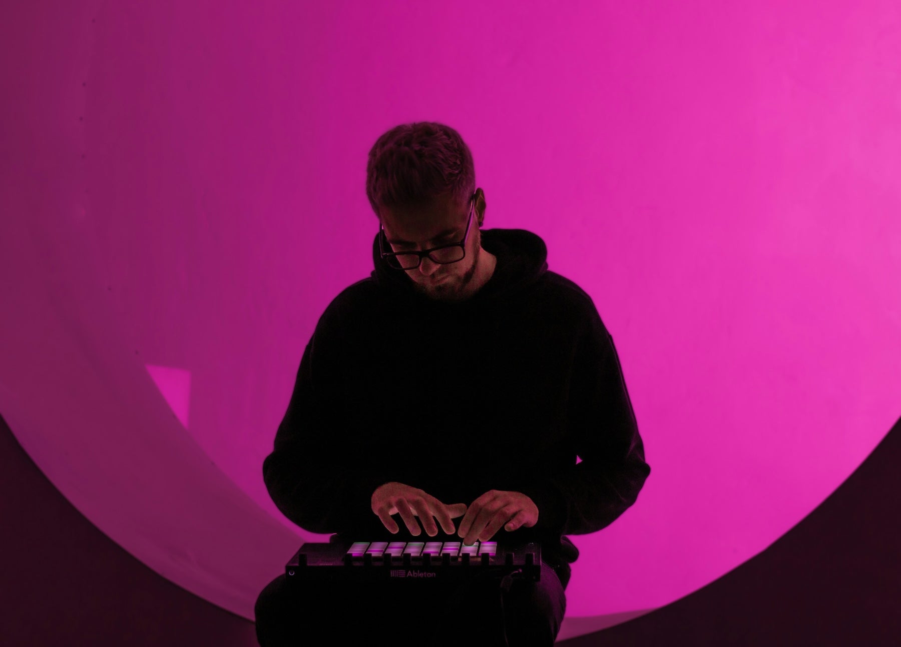 A producer working on synth patches in a DAW with headphones and a midi keyboard