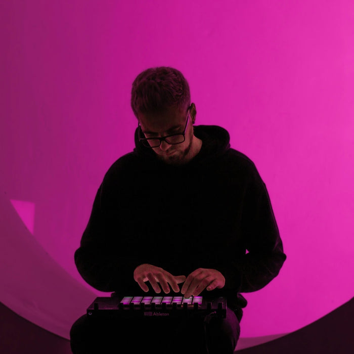A producer working on synth patches in a DAW with headphones and a midi keyboard